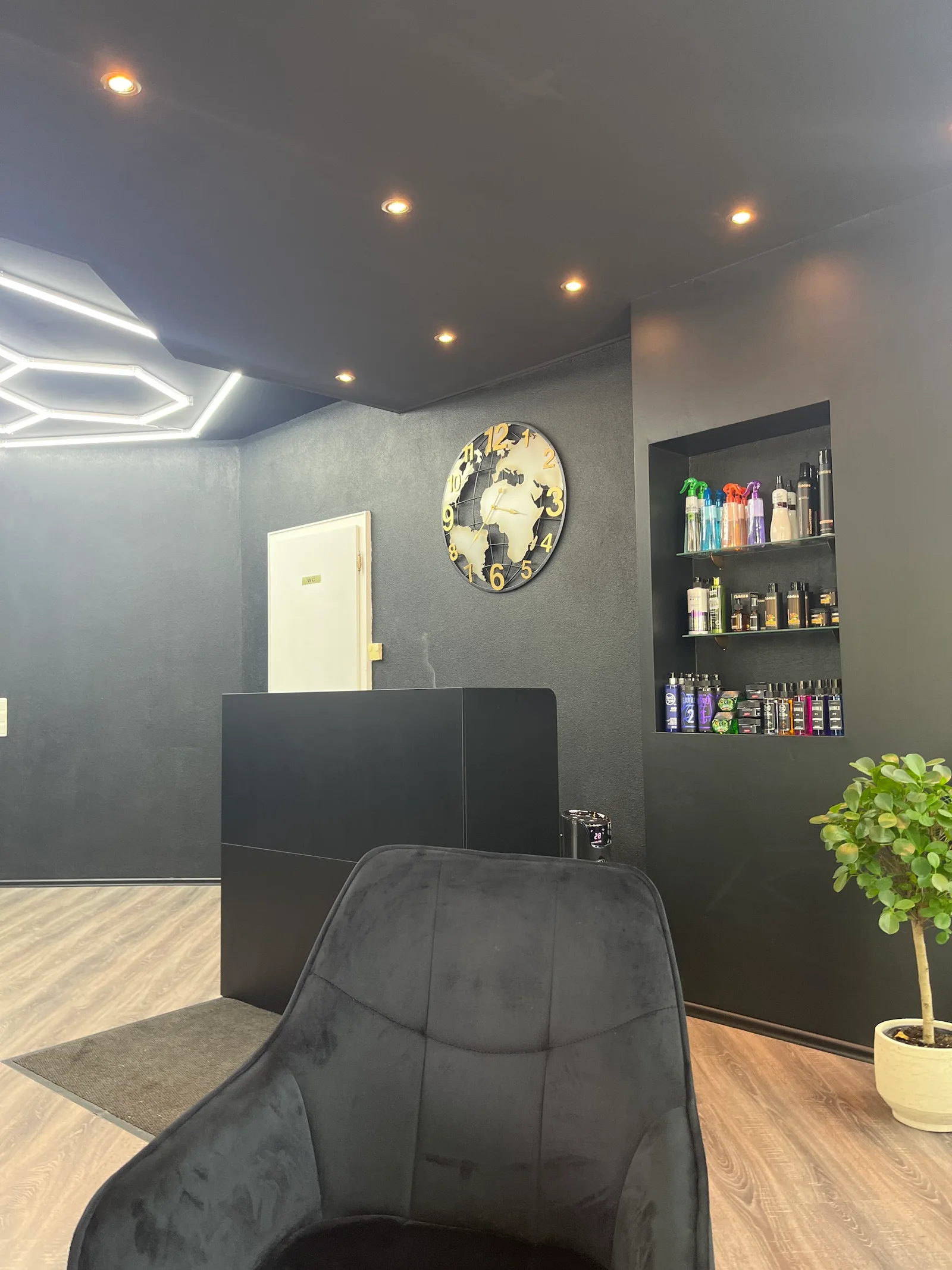 Empfangsbereich mit Tresen, großer Weltkarten-Uhr an der Wand und einem beleuchteten Regal mit Pflege- und Stylingprodukten